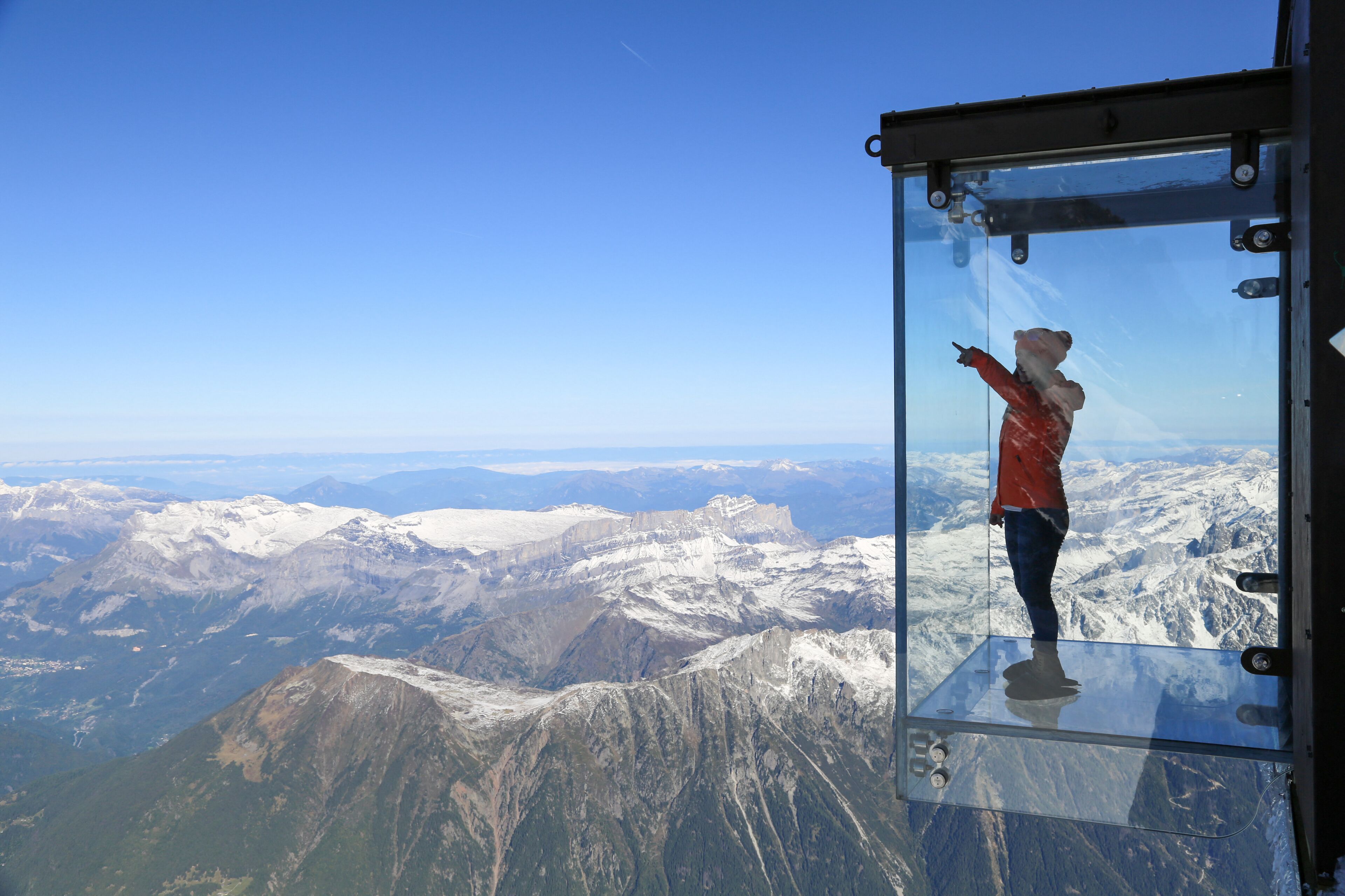 A person standing on a glass platform overlooking a mountainous landscape.