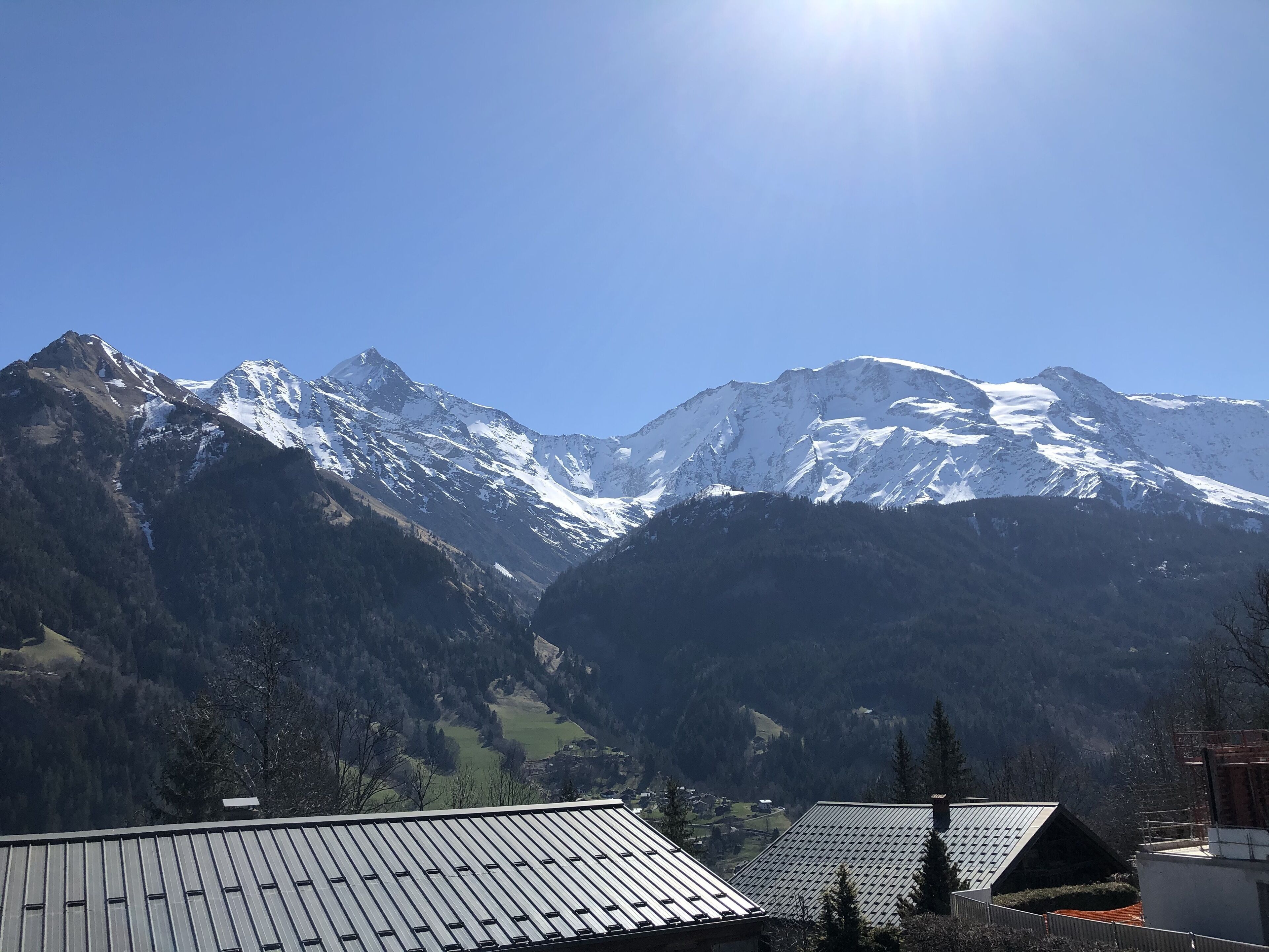 A mountain landscape with snow-capped peaks, a valley, and a building with a metal roof.