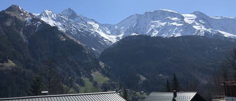 A mountain landscape with snow-capped peaks, a valley, and a building with a metal roof.
