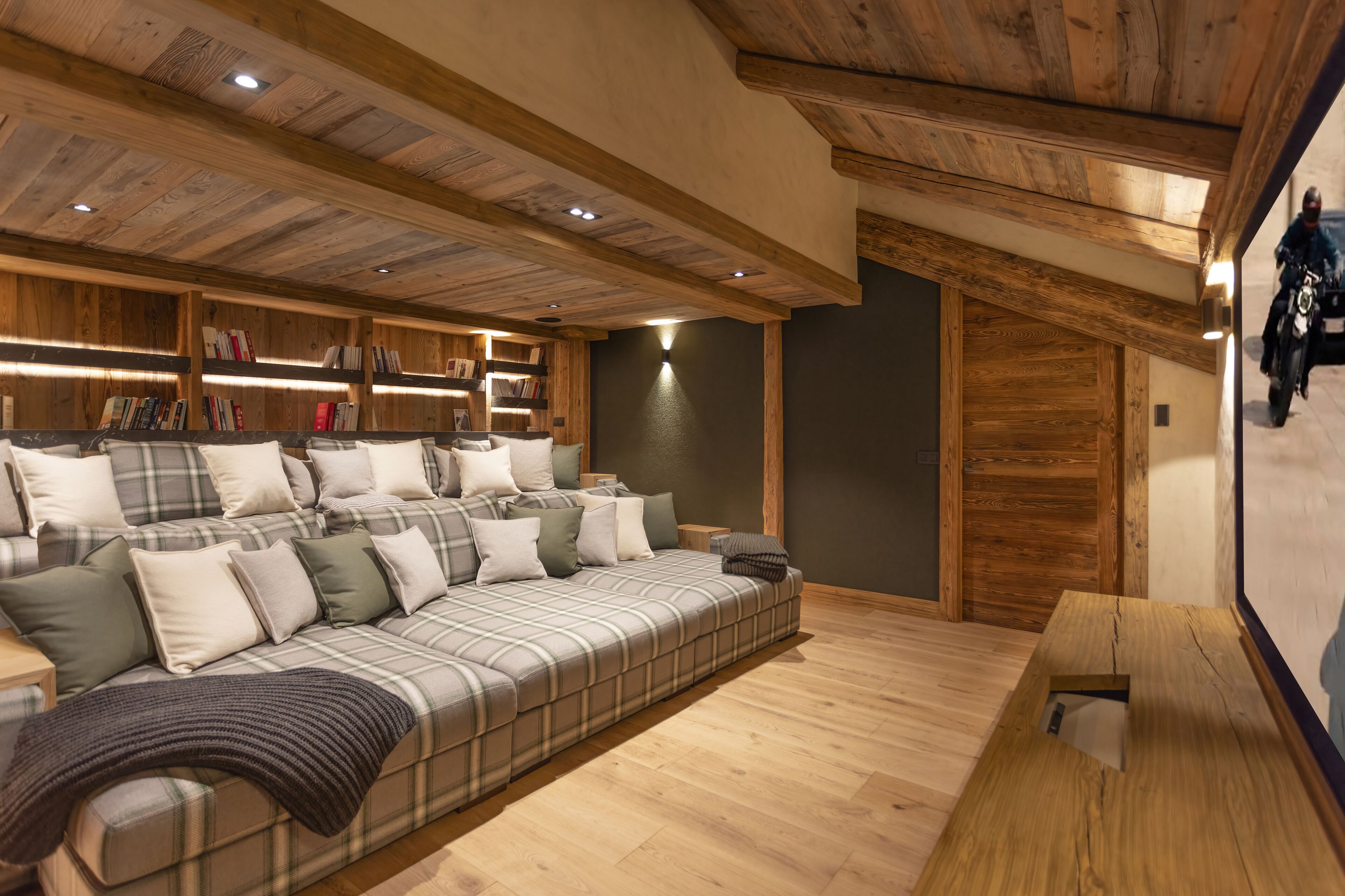 A cozy room with a large sofa, wooden bookshelves, and a wooden ceiling.
