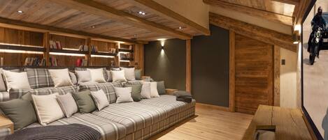 A cozy room with a large sofa, wooden bookshelves, and a wooden ceiling.