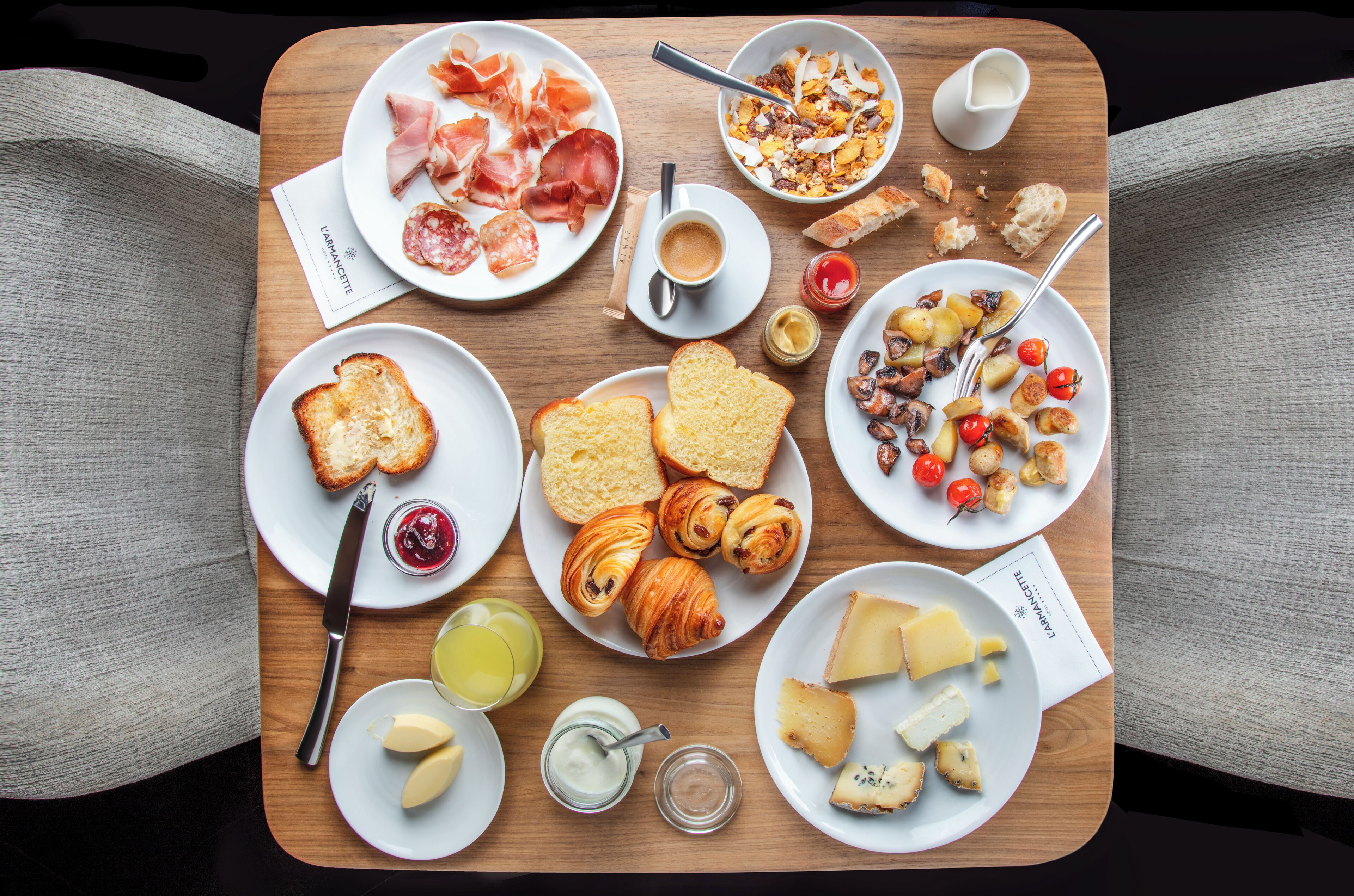 Una mesa de madera con diversos productos para el desayuno, como cruasanes, queso y pan.