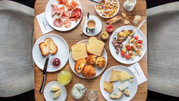 Una mesa de madera con diversos productos para el desayuno, como cruasanes, queso y pan.