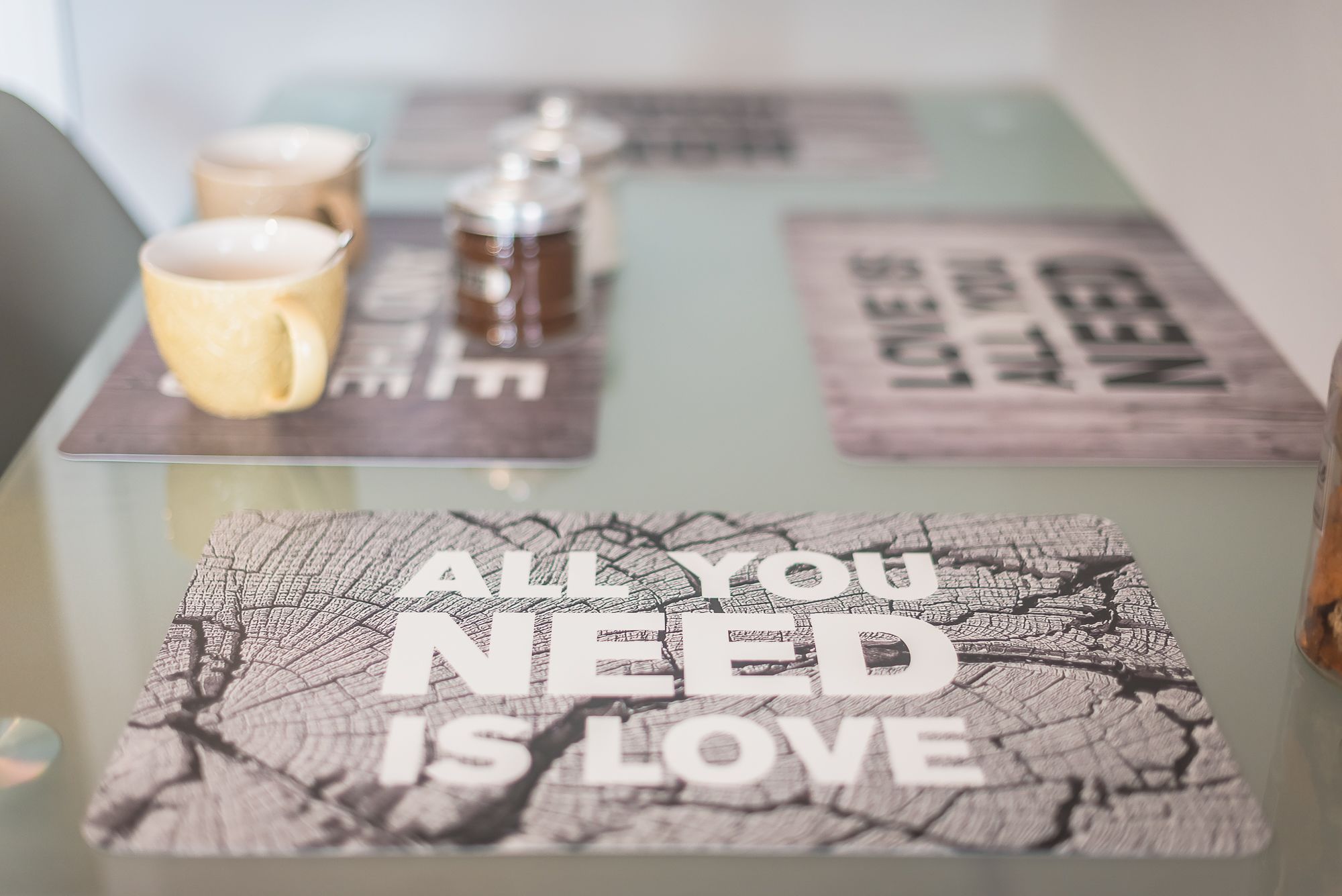 A table with a glass top displaying a message "ALL YOU NEED IS LOVE" and a cracked wood design. There are three cups on the table.
