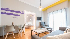 Ein modernes Wohnzimmer mit einer Couch, Sesseln, einem Couchtisch und einem an der Wand befestigten Fernseher.