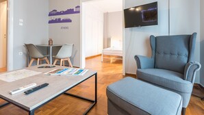 Ein modernes Wohnzimmer mit einem großen grauen Sessel, einem kleinen Tisch mit Fernbedienung und einer Wanddekoration mit Stadtansicht.