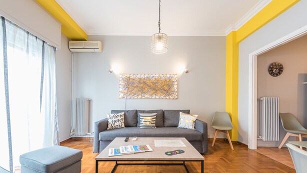 Ein modernes Wohnzimmer mit grauem Sofa, Couchtisch und einer Pendelleuchte.