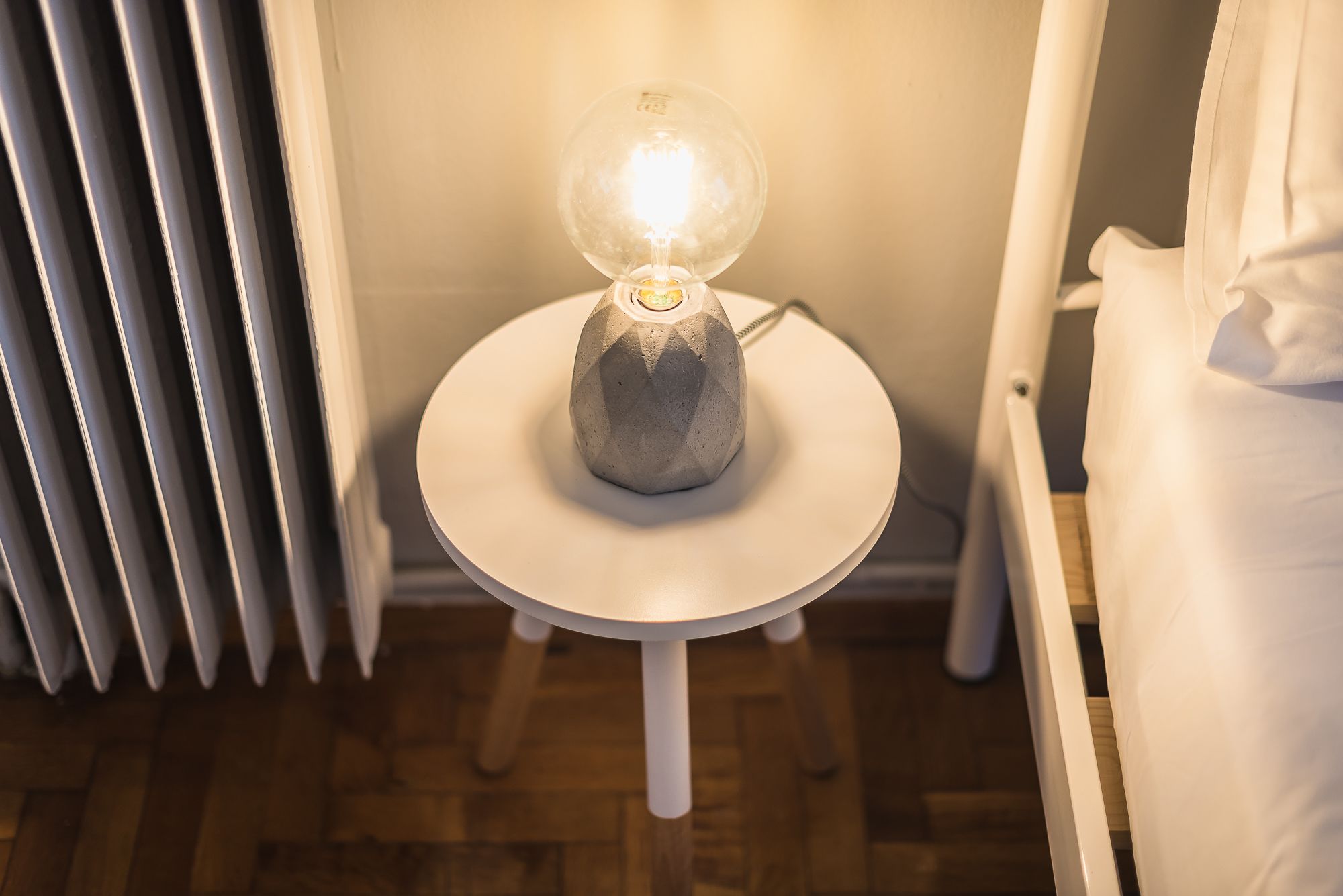 Eine moderne Lampe mit einer kugelförmigen Glasschirm auf einem weißen Podesttisch in einem Raum mit Holzboden und weißen Wänden.