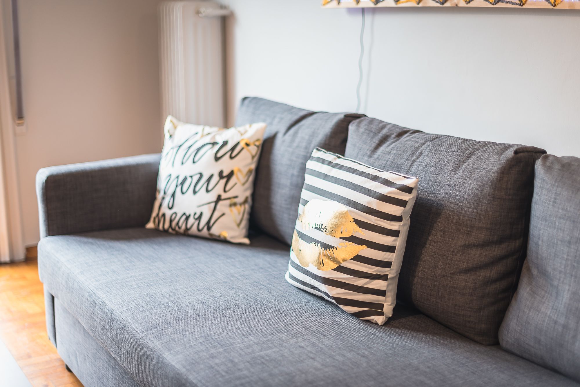 A grey sofa with two decorative pillows, one with a heart pattern and the other with a striped design.