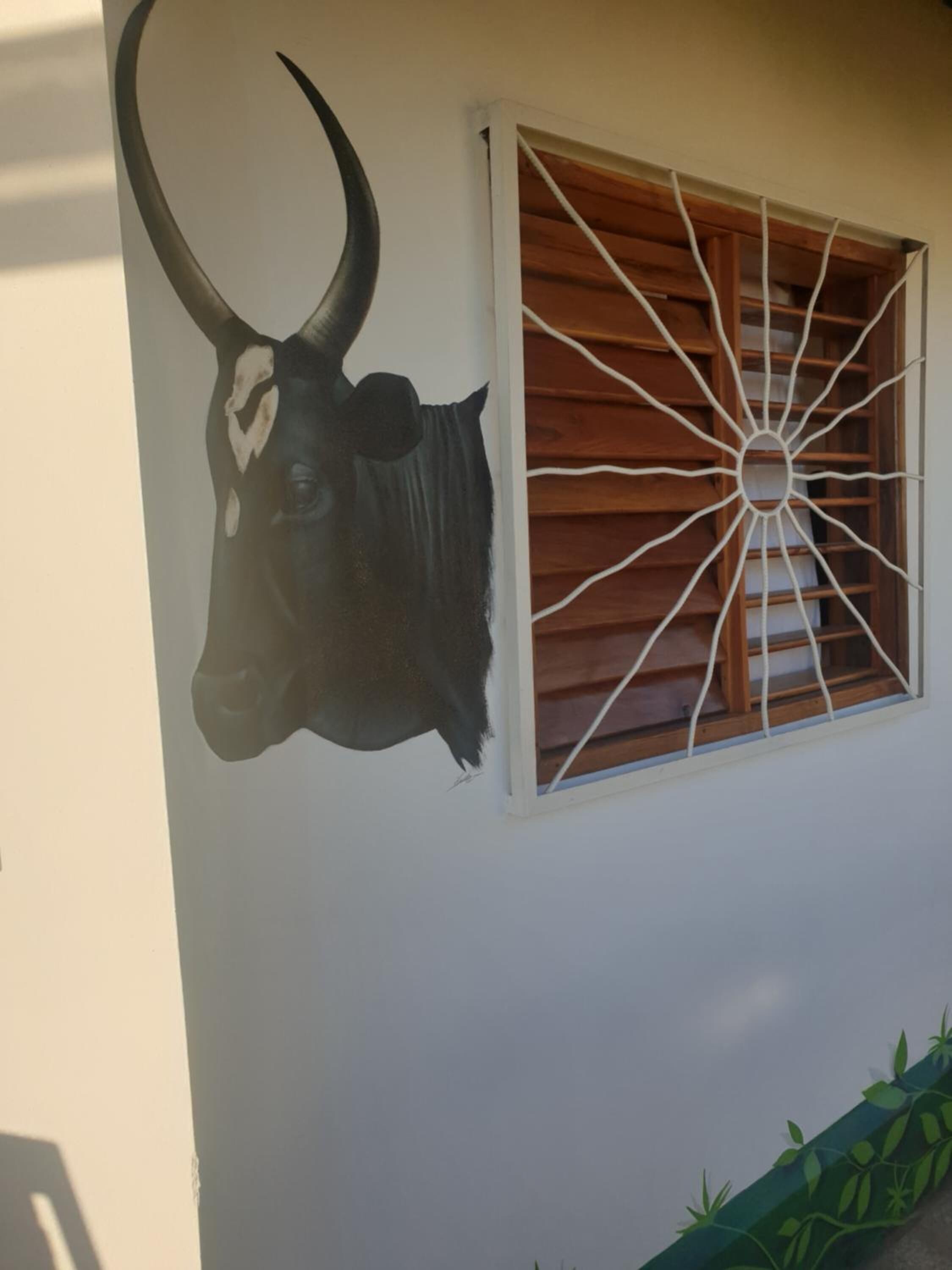Um mural com a cabeça de um touro numa parede de edifício, ao lado de uma janela com persianas de madeira.