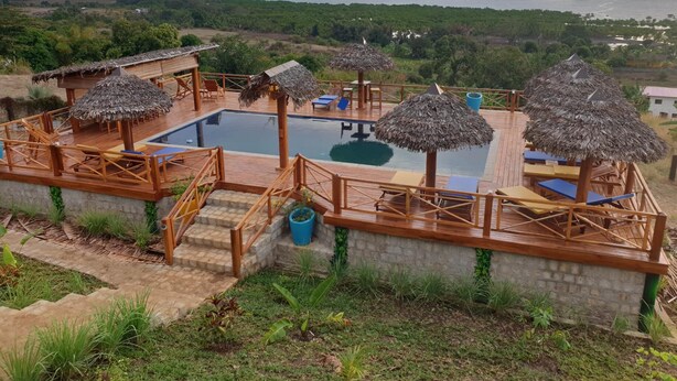 Un espace piscine doté d’une terrasse en bois, de parasols en chaume et de chaises longues.