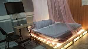 A room with a bed covered in a mosquito net, a desk with a computer, and a chair.