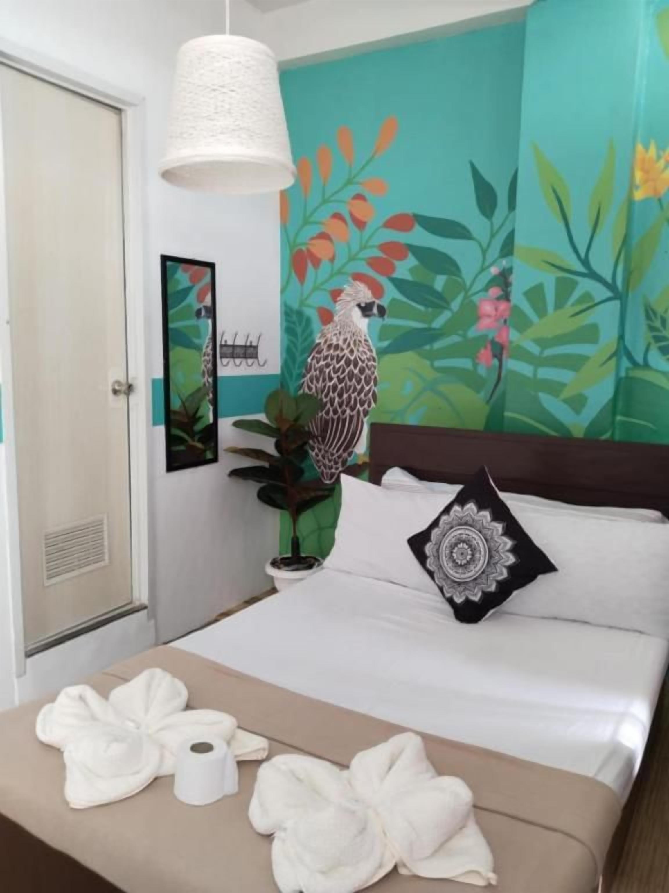 A hotel room with a bed, a bedside table with towels, a wall mural, and a hanging light fixture.
