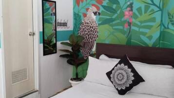 A hotel room with a bed, a bedside table with towels, a wall mural, and a hanging light fixture.