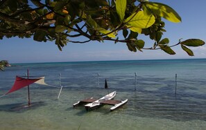 A small boat anchored near a clear blue sea, with a red canopy and a tree branch overhead. - Analatsara Eco Lodge (Nosy Nato)