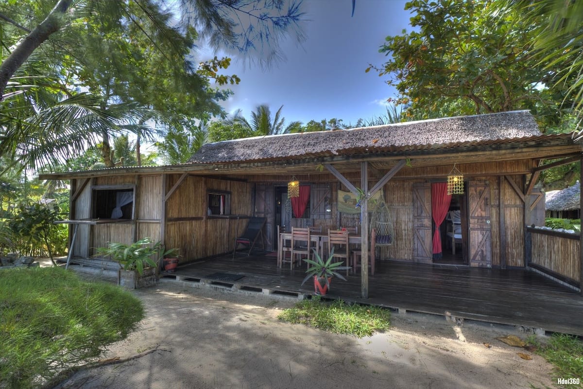 A rustic wooden building with a thatched roof, a porch with wooden chairs, and a small table.