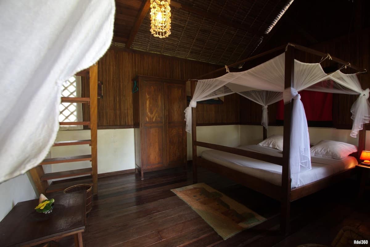 A wooden four-poster bed with a canopy, a wooden wardrobe, a small table with a decorative item, and a ladder against the wall.