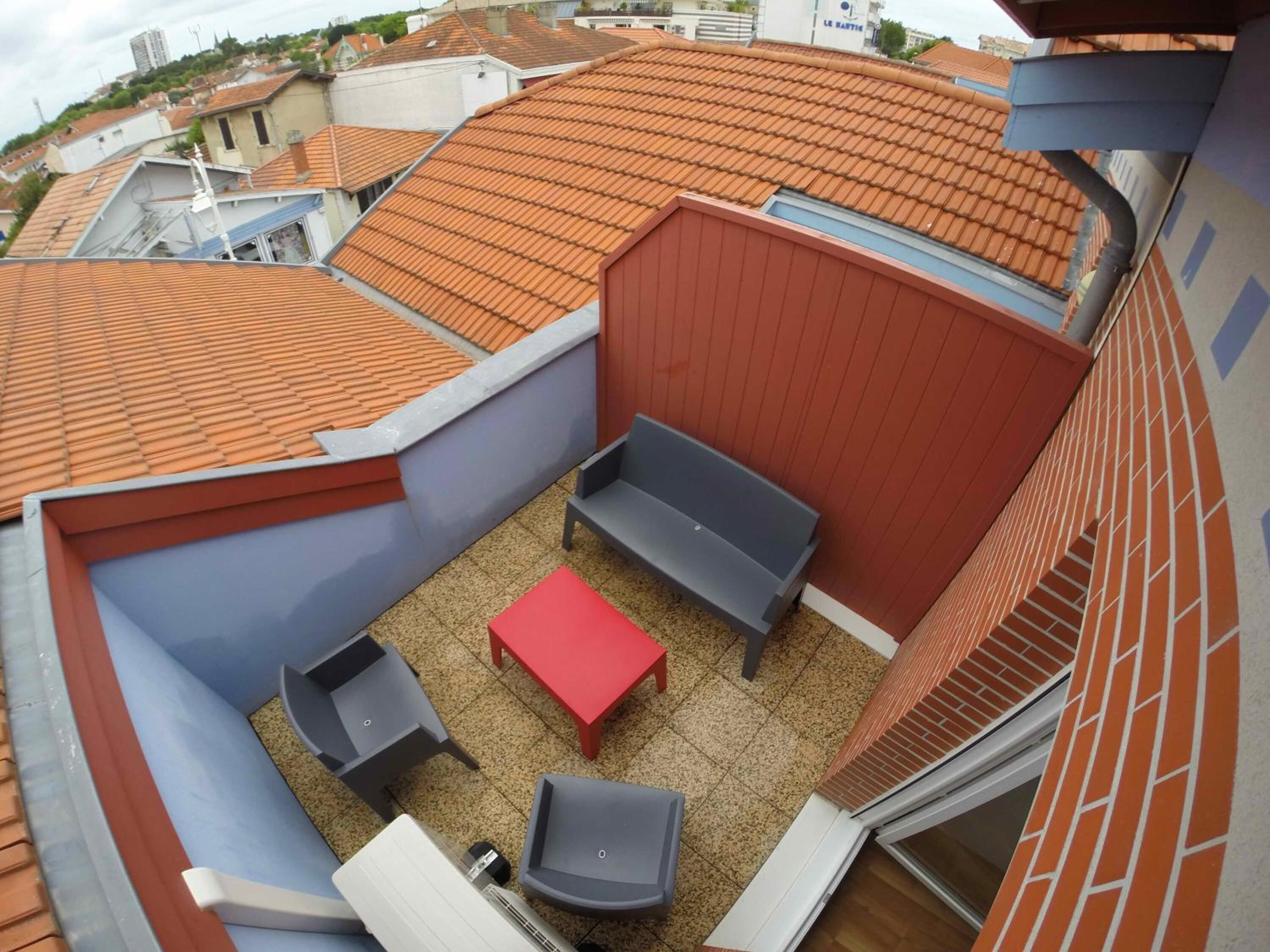 A rooftop terrace with a red table, two grey sofas, and a small table.