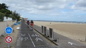 A wooden boardwalk leading to a beach with cyclists and a no-entry sign for vehicles. - Weekend Hotel Les Pieds dans l'Eau (Viviers-du-Lac)