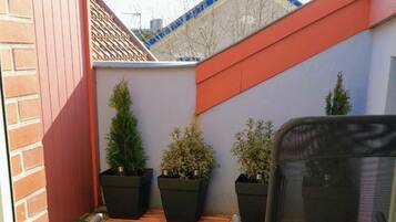 Un petit espace extérieur clos, doté d’un gazon synthétique, de deux plantes en pot et d’une chaise de bureau noire.