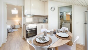 A modern kitchen with white cabinets, a built-in oven, and a dining area with a wooden table set for two. - Avenida apartement (Braga)