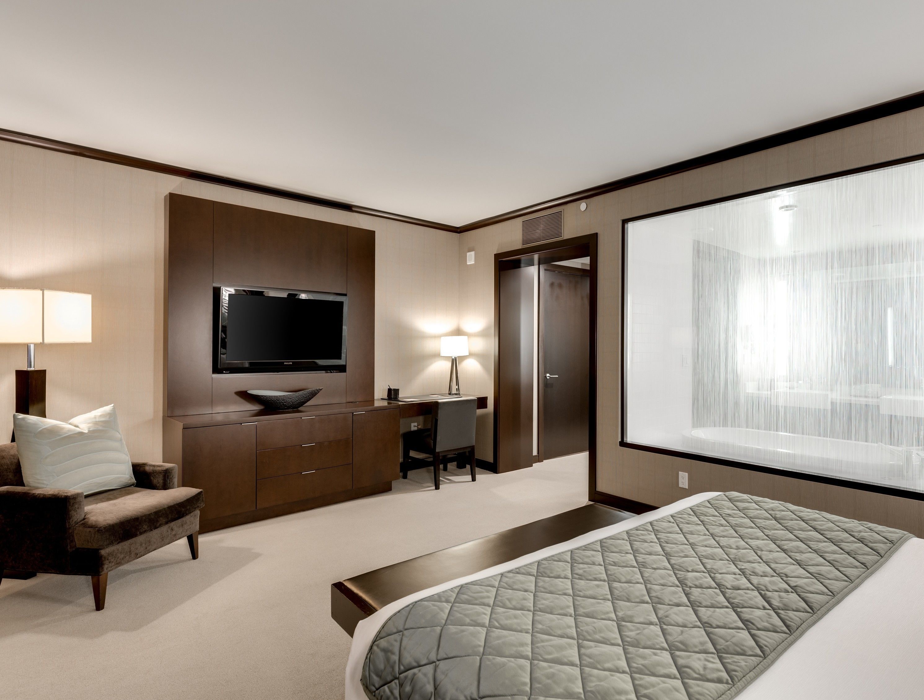 Moderni hotellihuone, jossa on suuri sänky, työpöytä, televisio ja suuri ikkuna.