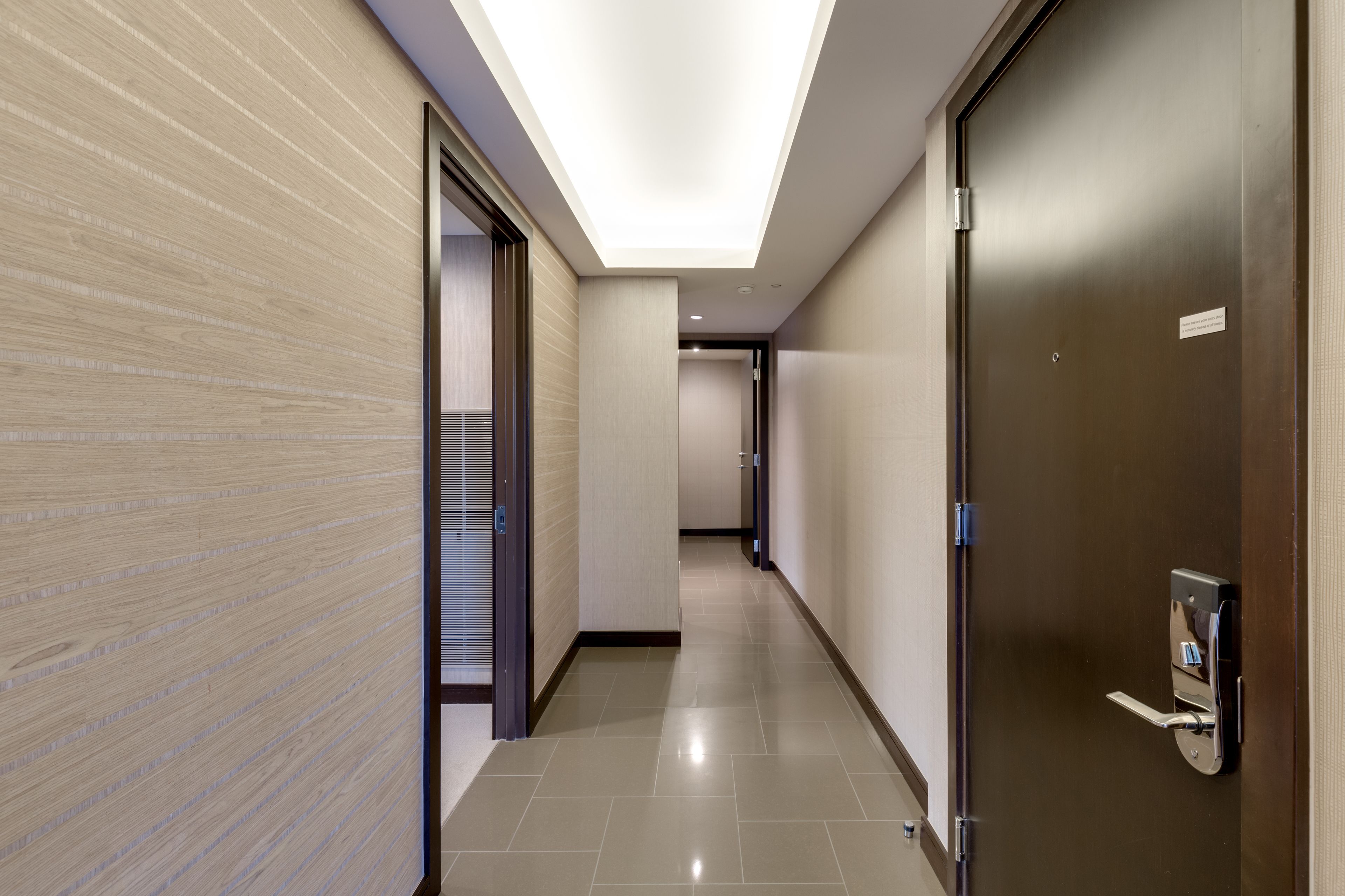 A modern hallway with a wooden wall, a ceiling light, and a door with a handle.