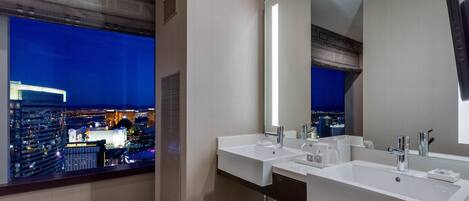 Un baño moderno con dos lavamanos, un espejo grande y vistas a un paisaje urbano nocturno.