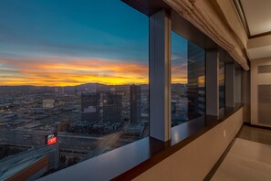 A modern hotel room with a large window offering a cityscape view during sunset. - Secret Suites at Vdara (Las Vegas)