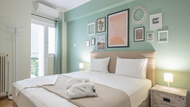 A neatly made bed with a white comforter and two pillows, a bedside table with a lamp, and a wall with several framed pictures. - Boutique Acropolis Apartment  by Cloudkeys (Athens)