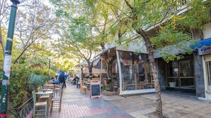 A pedestrian street lined with cafes and shops, featuring outdoor seating and a tree-lined path. - Boutique Acropolis Apartment  by Cloudkeys (Athens)