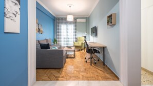 A modern living room with a grey sofa, a wooden coffee table, and a yellow armchair. There is a desk with a chair and a lamp. The room has blue walls and a wooden herringbone floor. - Boutique Acropolis Apartment  by Cloudkeys (Athens)
