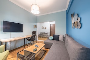 A modern living room with a flat-screen TV, a wooden coffee table, a gray sofa, and a blue accent wall. - Boutique Acropolis Apartment  by Cloudkeys (Athens)