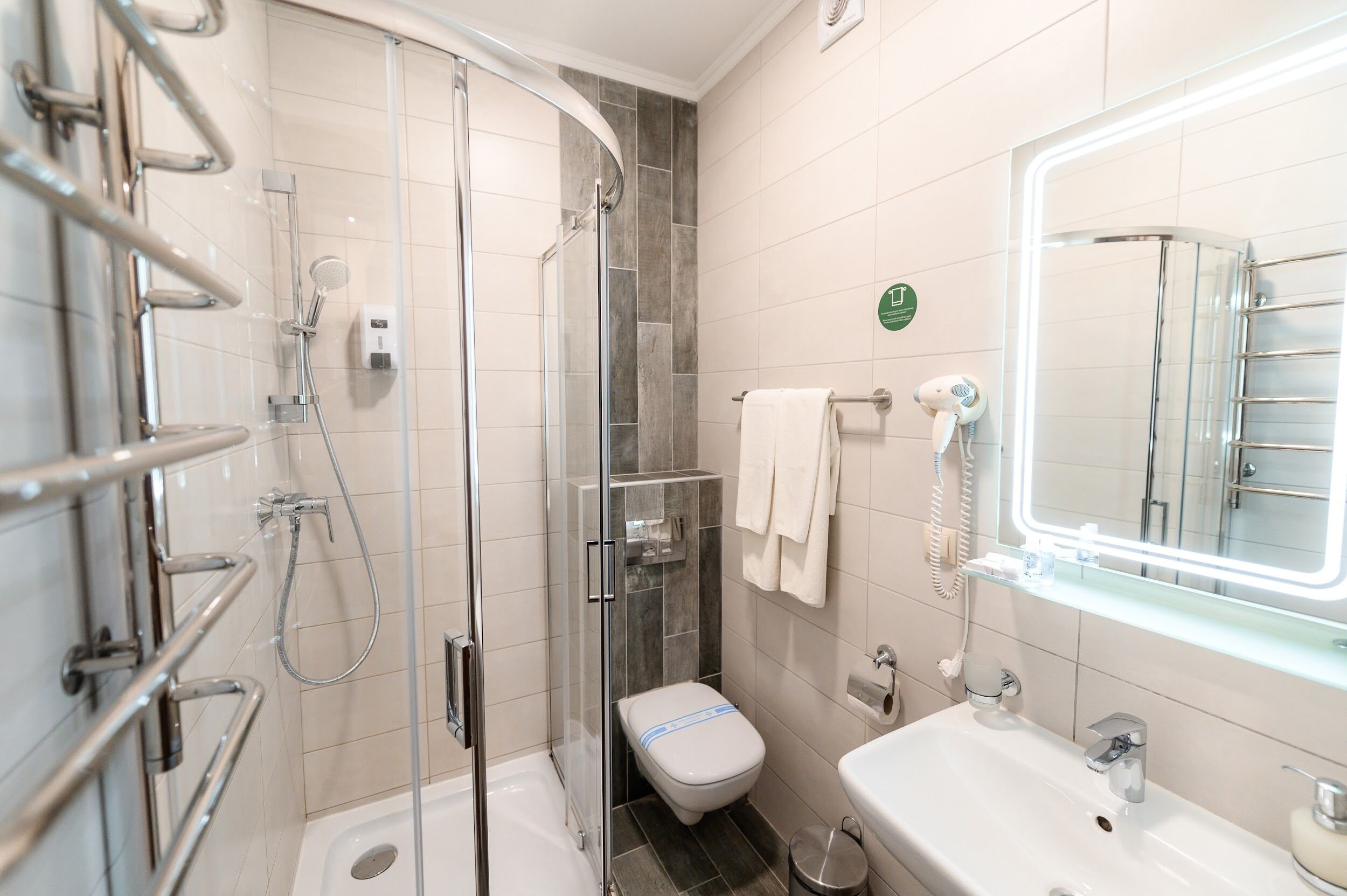 Un baño moderno con ducha envuelta en vidrio, lavamanos blanco e iluminación LED en el espejo.