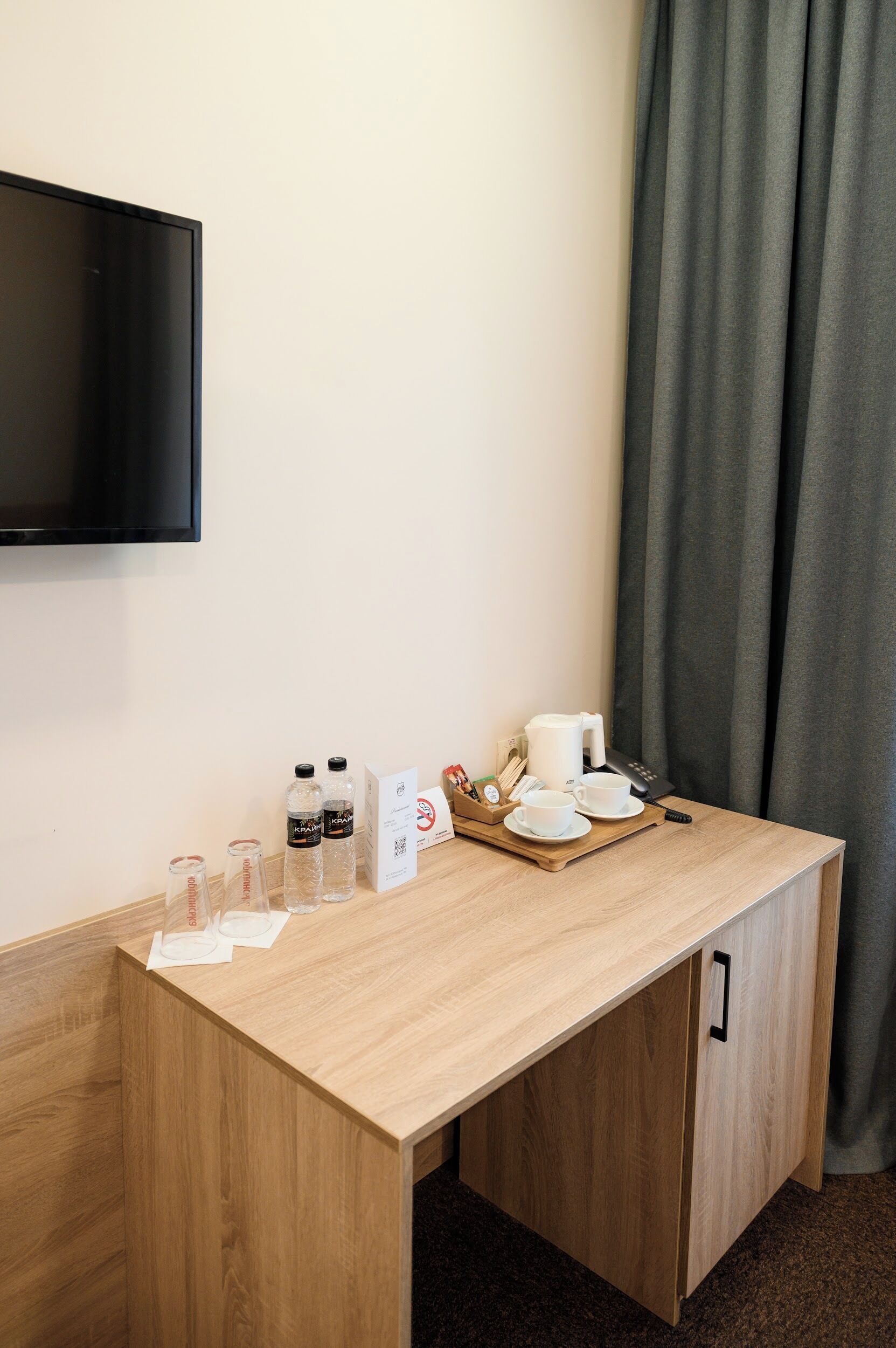 A hotel room with a wooden desk, a flat-screen TV mounted on the wall, a tray with a coffee maker, cups, and a phone.