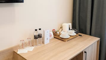 A hotel room with a wooden desk, a flat-screen TV mounted on the wall, a tray with a coffee maker, cups, and a phone.