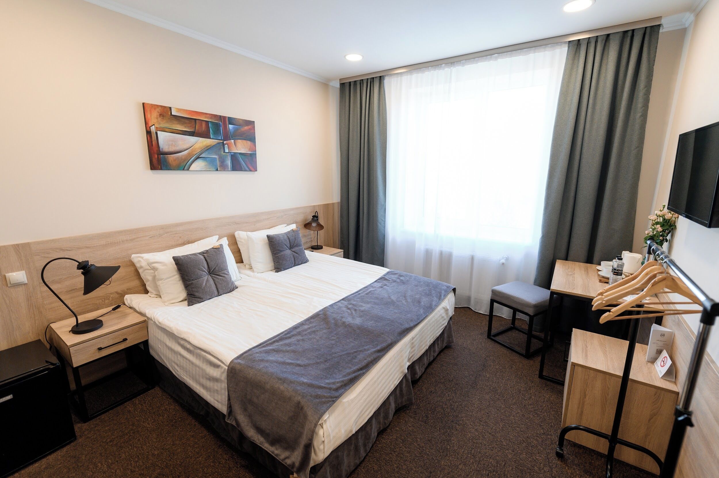 Habitación de hotel con cama, mesitas de noche, escritorio, silla, televisor y ventana con cortinas.