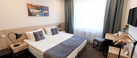 Habitación de hotel con cama, mesitas de noche, escritorio, silla, televisor y ventana con cortinas.
