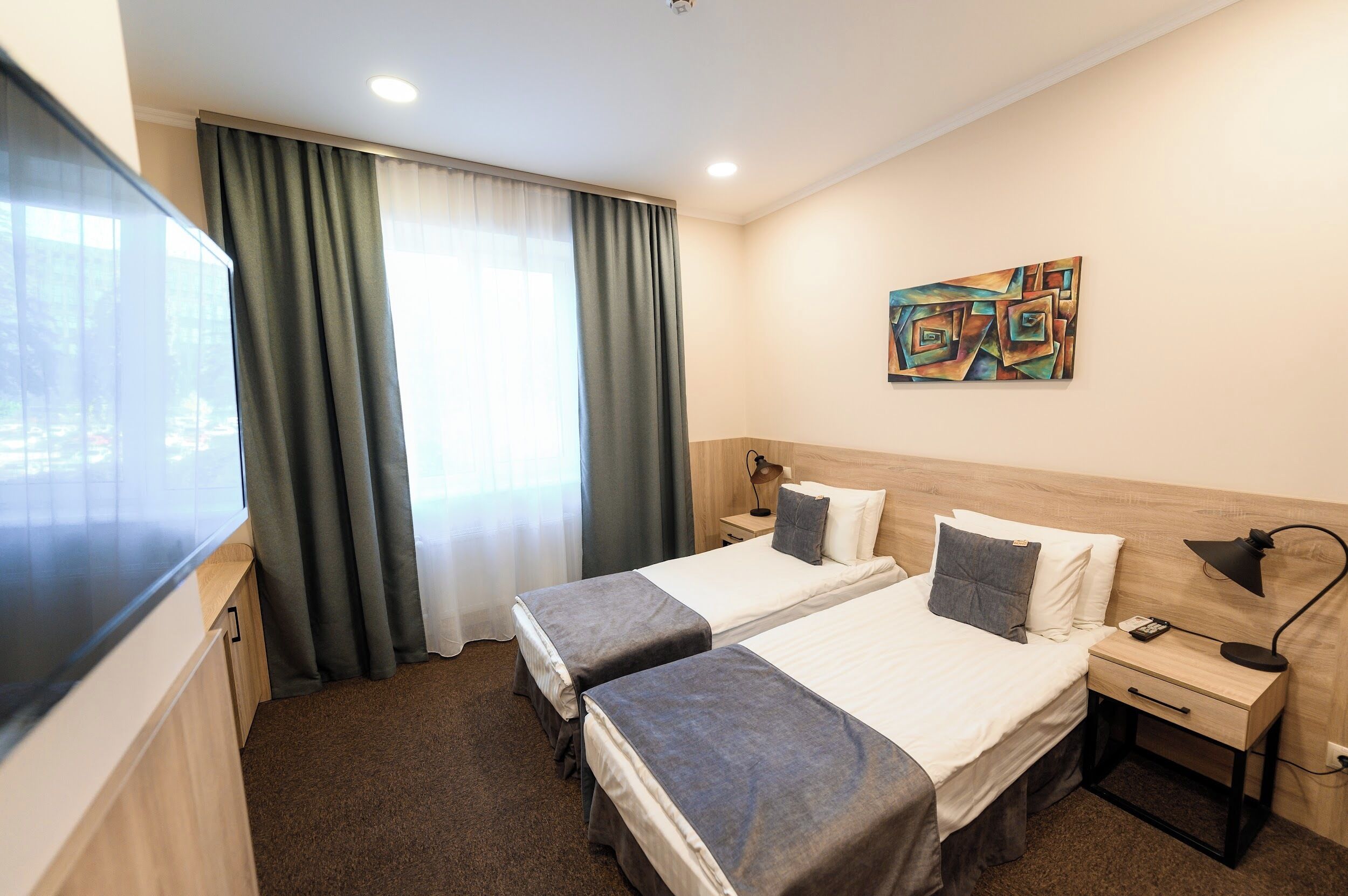 Ein Hotelzimmer mit zwei Betten, einem Fernseher, einem Gemälde und einem Fenster mit Vorhängen.