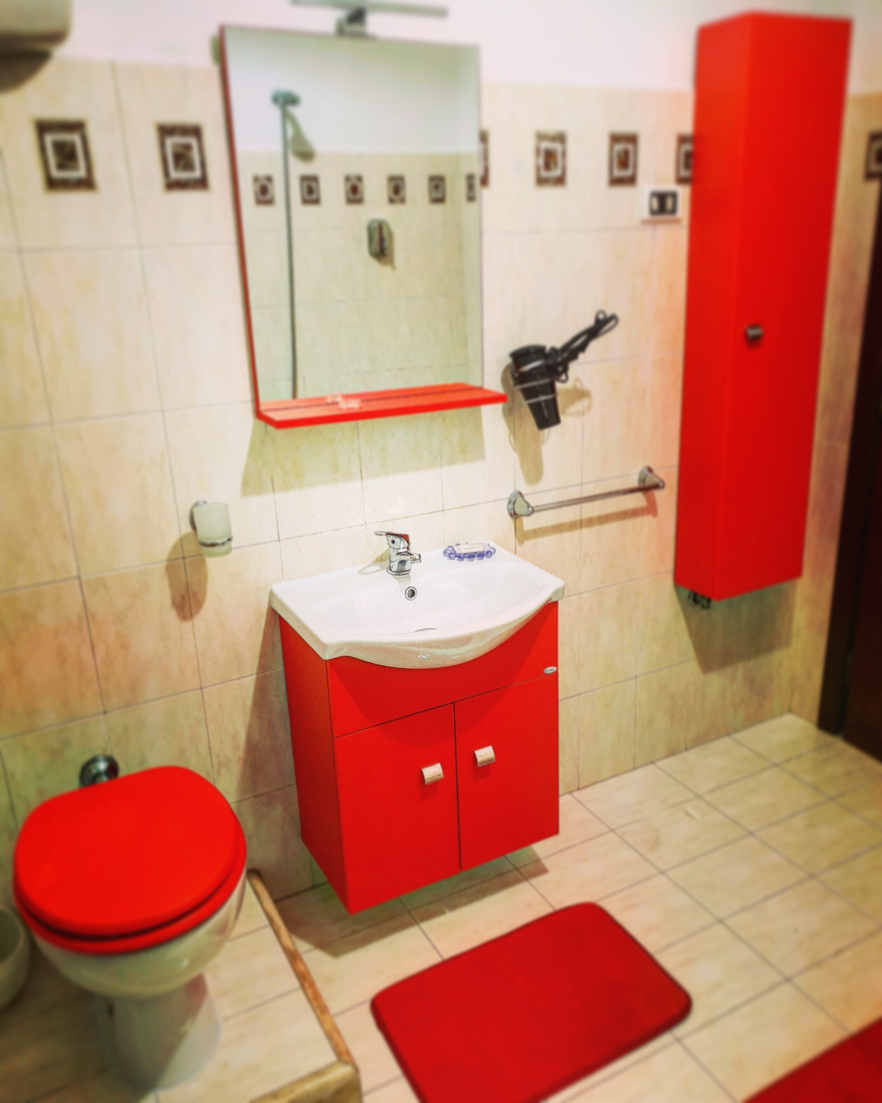 A bathroom with a red sink, toilet, and cabinet, a mirror above the sink, and a red mat on the floor.