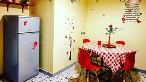 A kitchen with a refrigerator, a dining table with a checkered tablecloth, red chairs, and wall decorations including a clock and motivational phrases. - Central Isernia (Isernia)