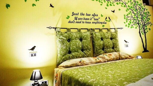 A bedroom with a green patterned bedspread, a tufted headboard, and a wall decal of birds and a tree. - Central Isernia (Isernia)