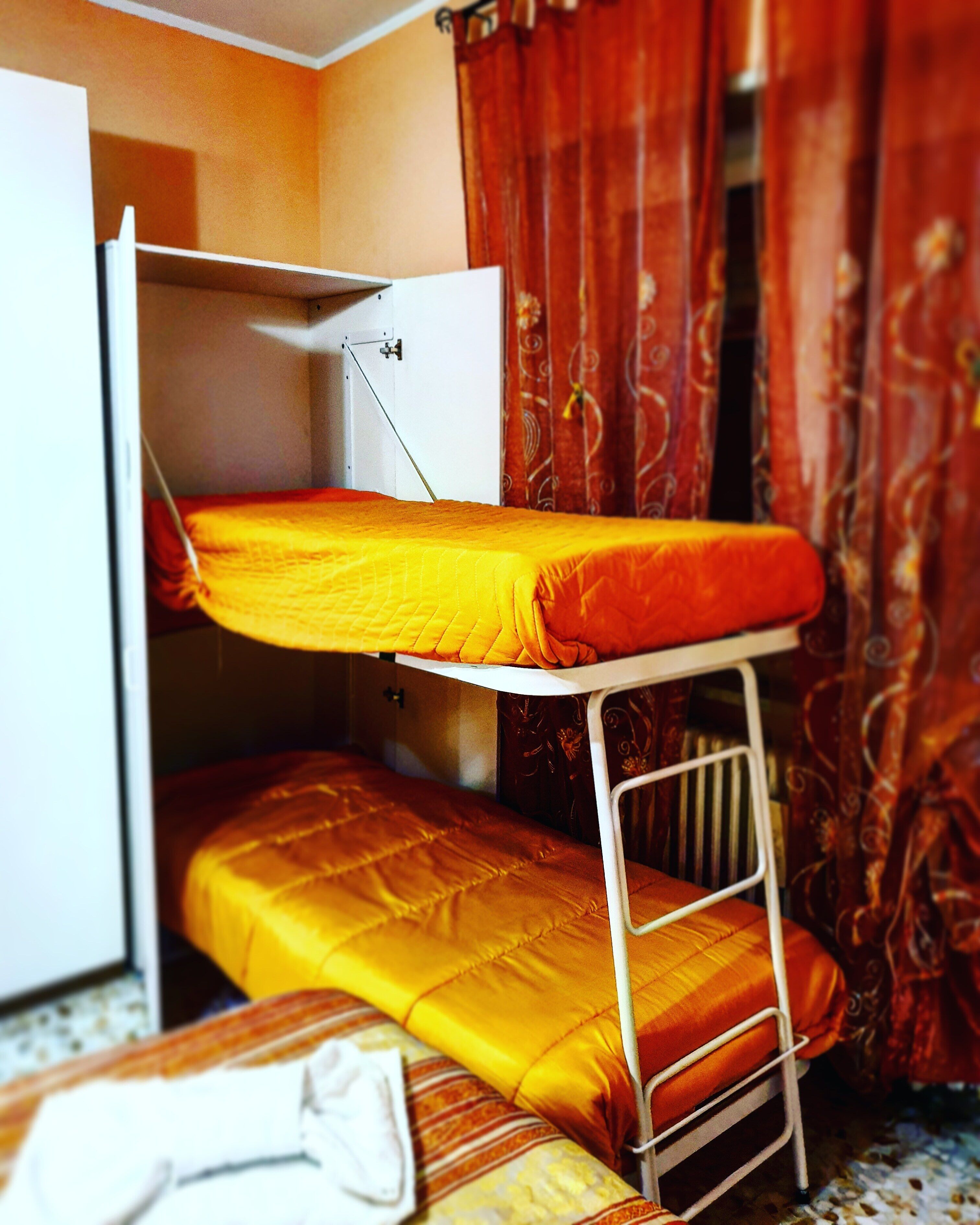 Una cama litera con estructura metálica blanca, una cama inferior con colcha amarilla y un armario blanco con la puerta entreabierta.