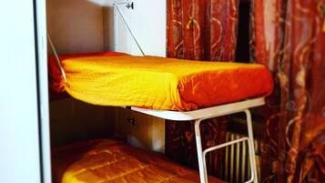 Una cama litera con estructura metálica blanca, una cama inferior con colcha amarilla y un armario blanco con la puerta entreabierta.