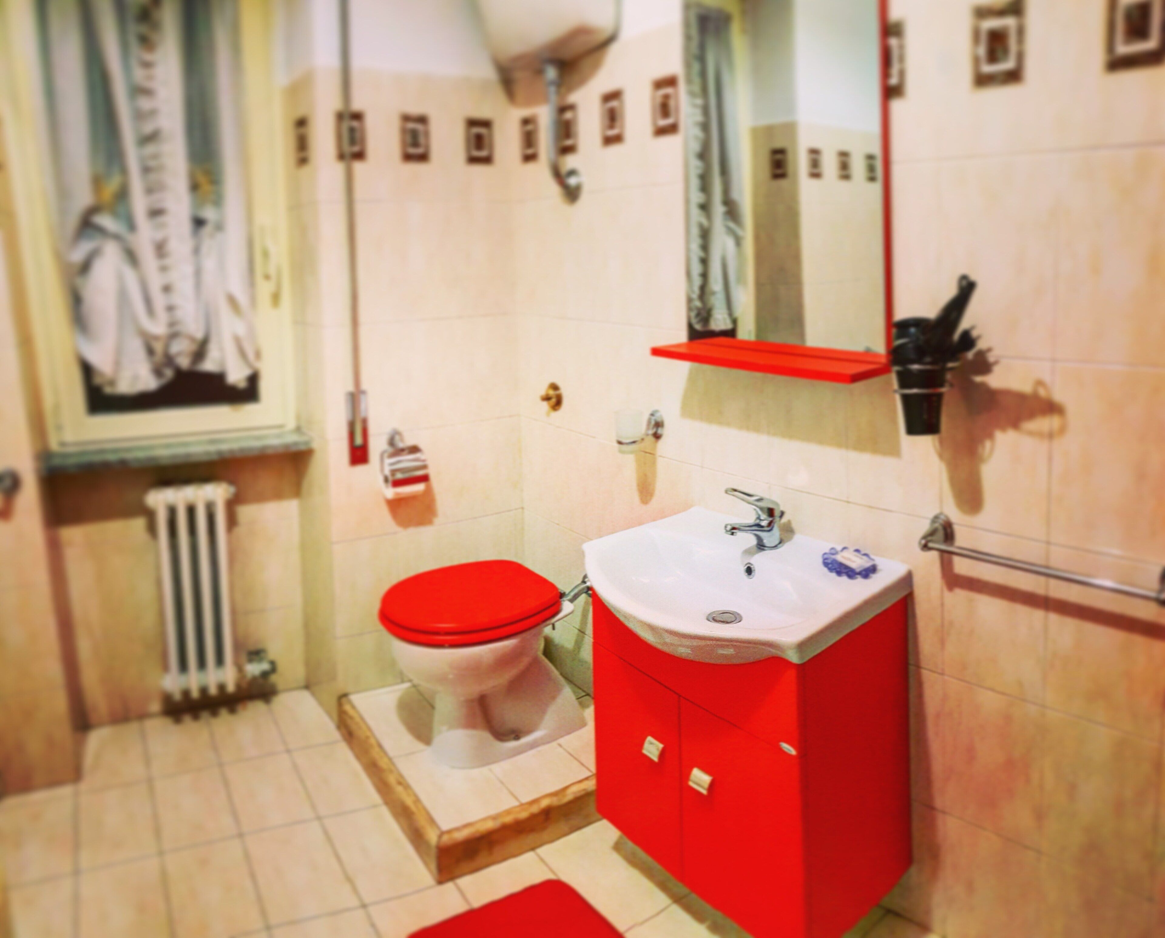 A bathroom with a red toilet, a white sink, and a red cabinet.
