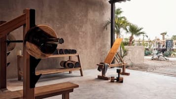 A gym with wooden equipment, a concrete floor, and a view of palm trees and rocks outside.