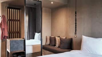 A modern hotel room with a large bed, a smaller bed, and a seating area with cushions.