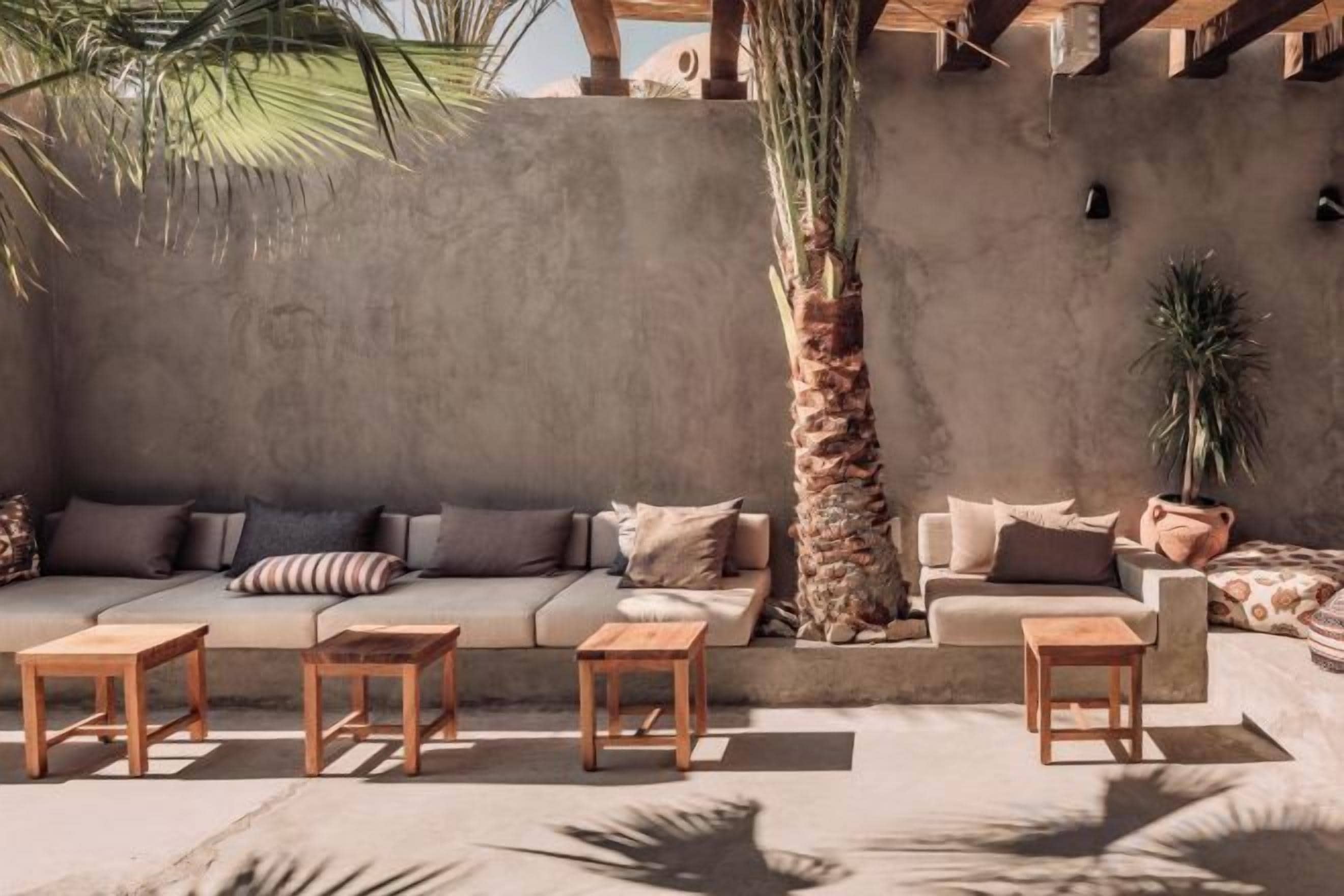 Un espacio al aire libre iluminado por el sol con un sofá, dos sillones y tres mesas de madera.