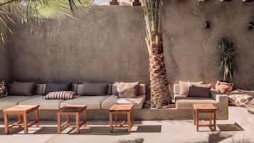 Un espacio al aire libre iluminado por el sol con un sofá, dos sillones y tres mesas de madera.