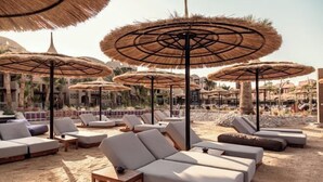 Un área de descanso en la playa con varias tumbonas y sombrillas de paja.